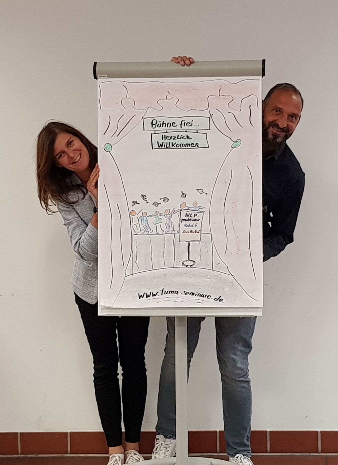 Maja und Tunç Gültekin hinter einem Flipchart mit Willkommens-Skizze zur NLP-Practitioner-Ausbildung
