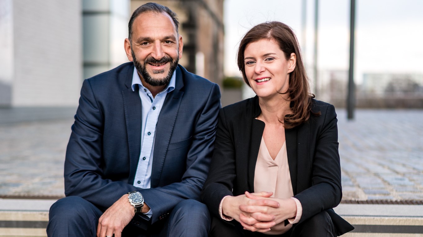 Maja und Tunç Gültekin sitzen lachend nebeneinander vor den Kranhäusern in Köln